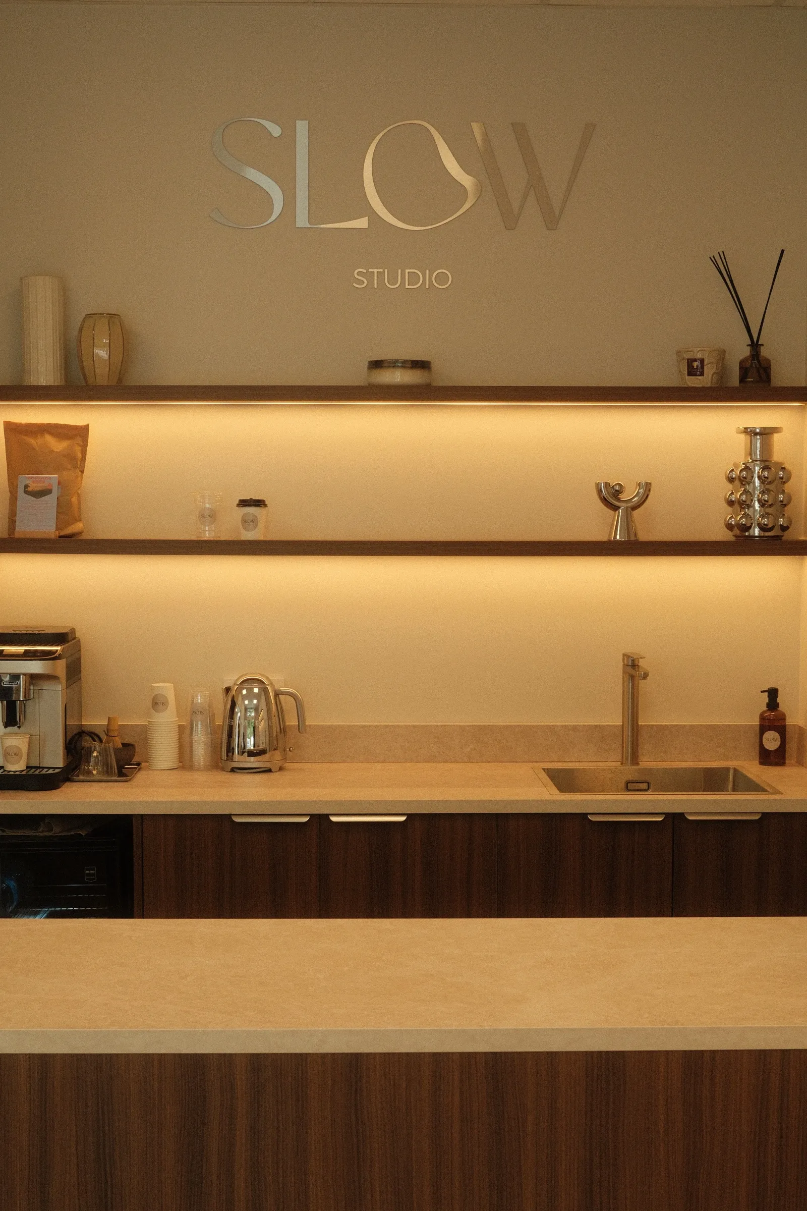Le comptoir d'accueil du studio, surmonté de l'enseigne murale Slow Studio et d'étagères en noyer rétroéclairées.