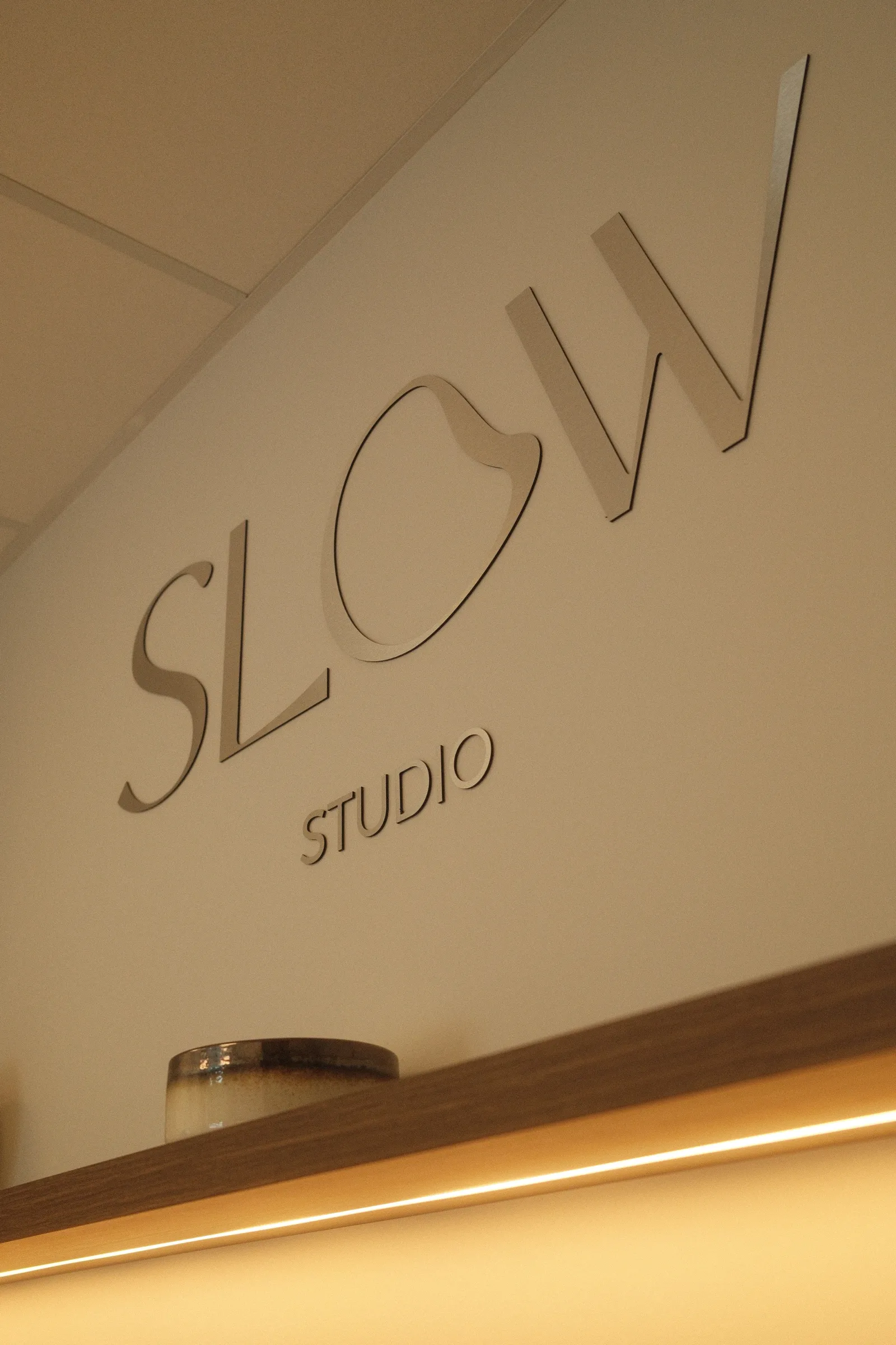 L'enseigne Slow Studio en lettres métal sur le mur grège de l'accueil, éclairée par un bandeau LED.