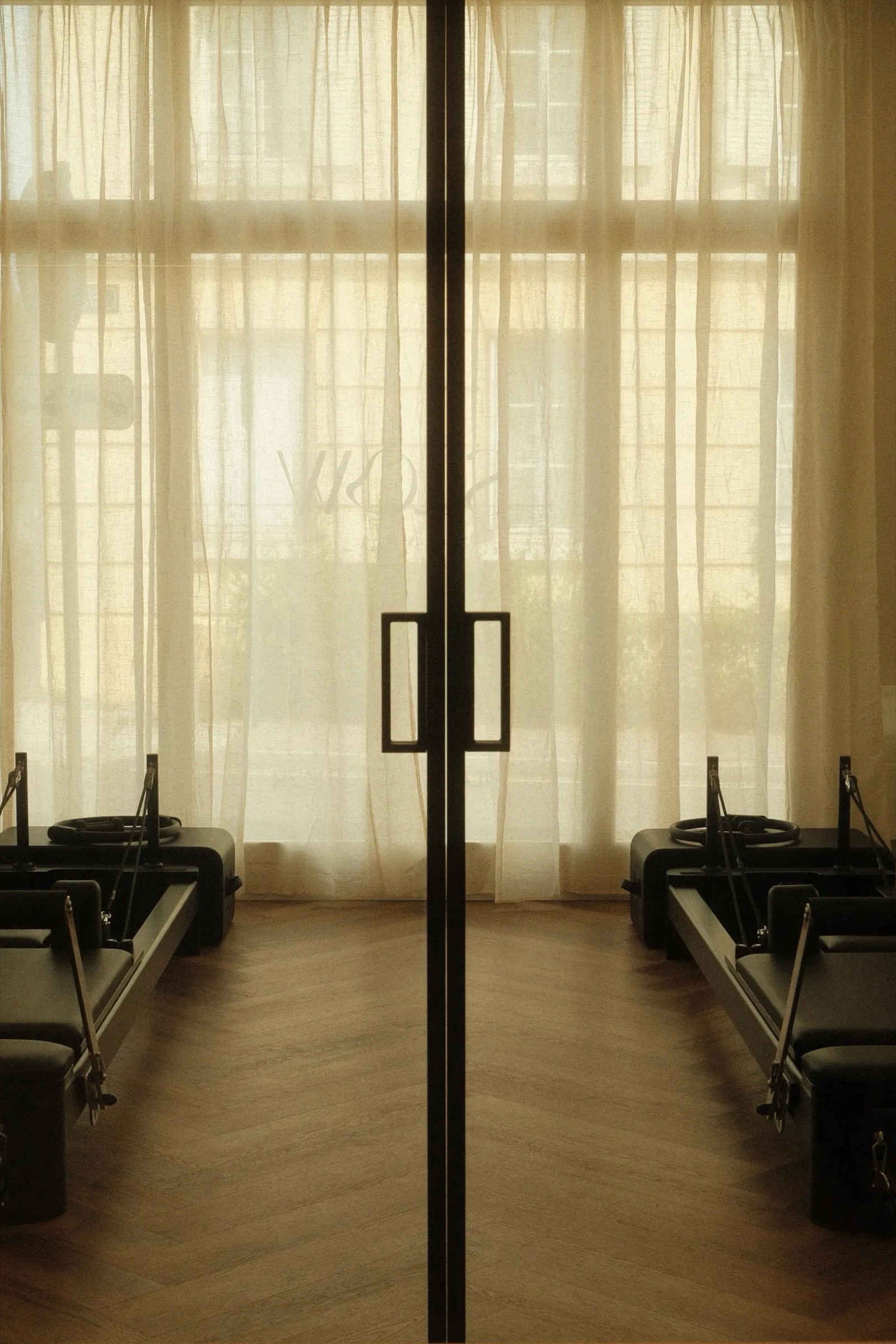 La double porte vitrée de la salle, ouverte sur les Reformers et les rideaux de lin baignés de lumière.