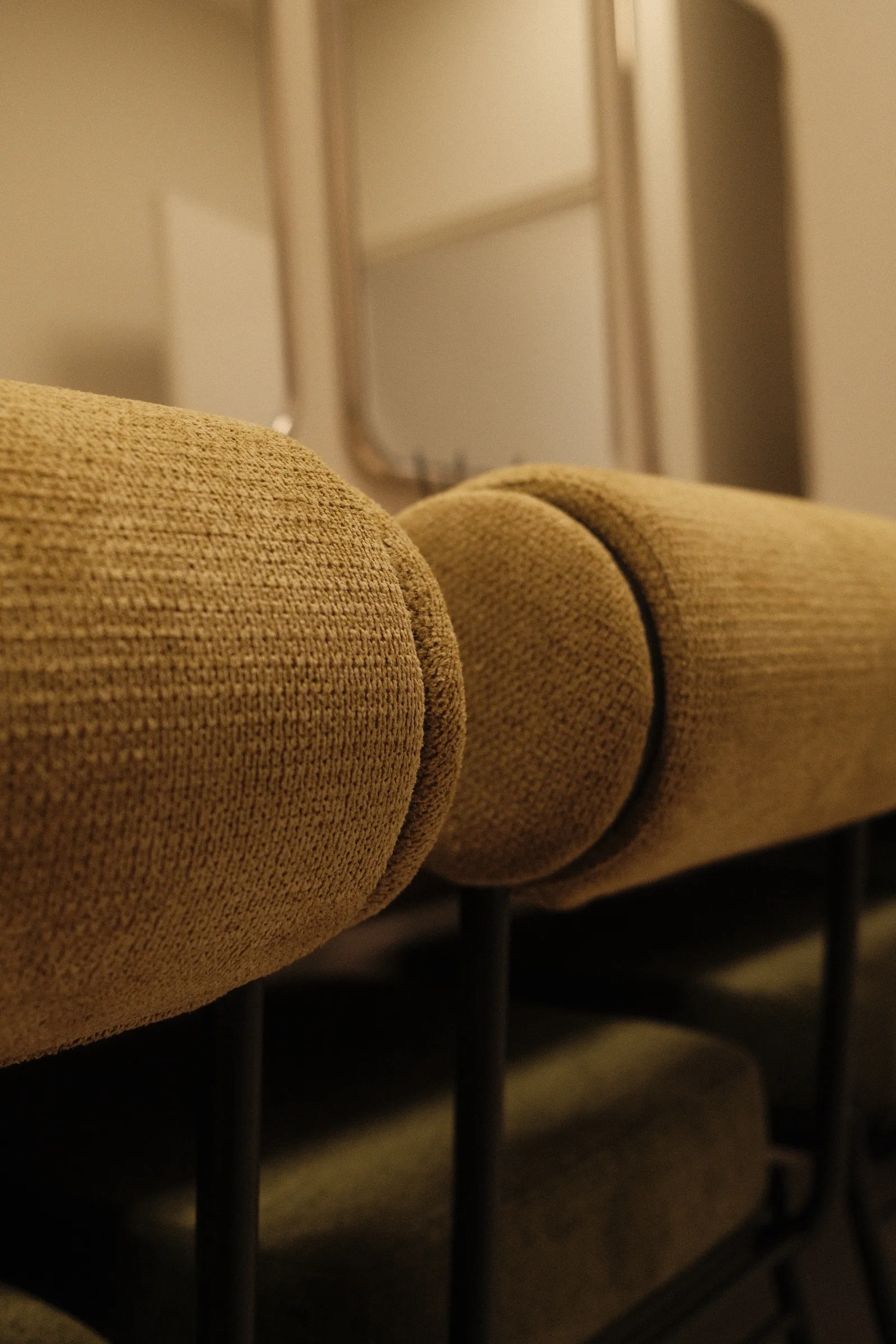 Traversins en bouclette moutarde alignés sur les assises du vestiaire.