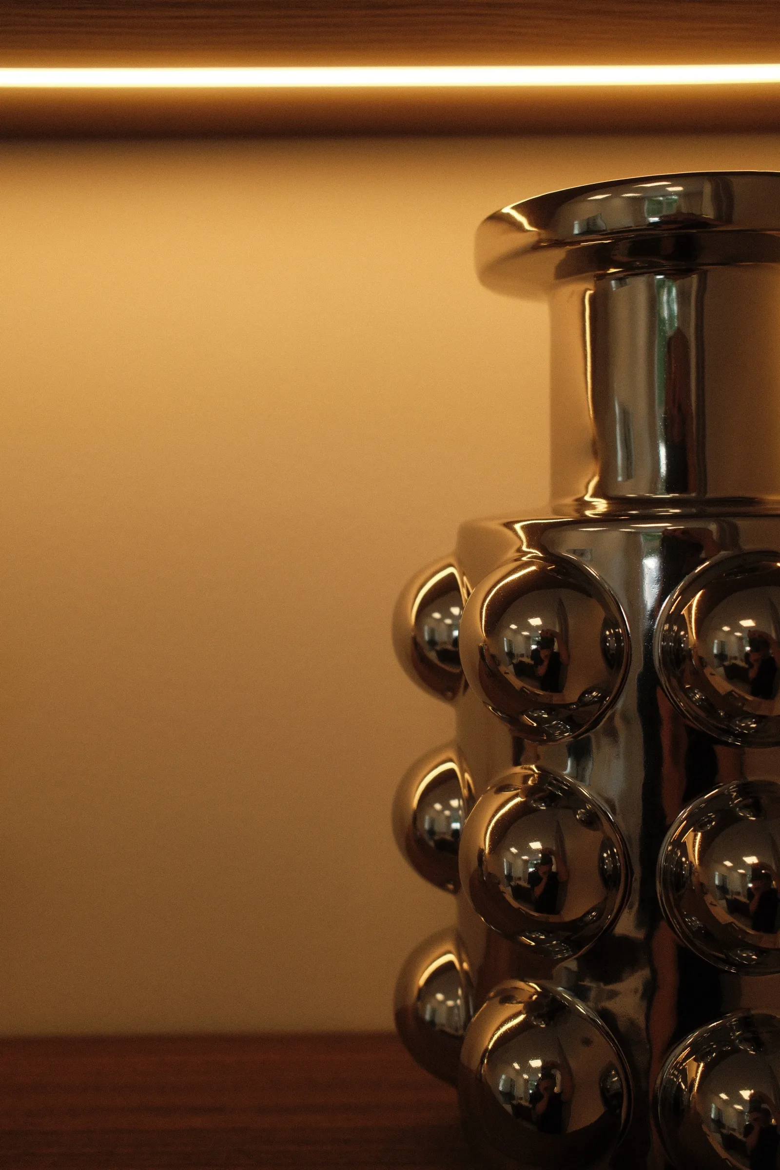 Vase chromé à motif de billes posé sur une étagère du studio.